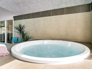 A hot tub in a room with tiled walls and a glass door leading to a kitchen area.