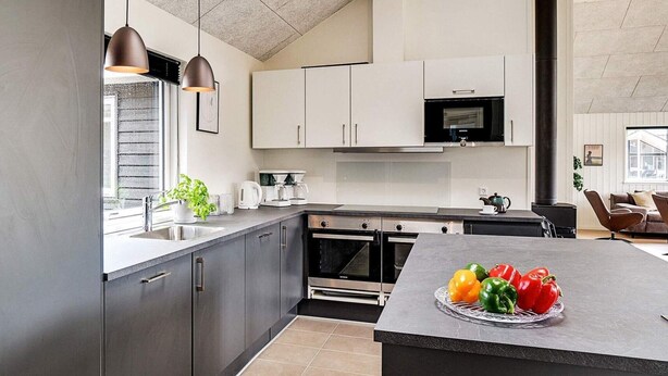 Una cocina moderna con armarios oscuros, electrodomésticos de acero inoxidable y una isla central con fruteros.