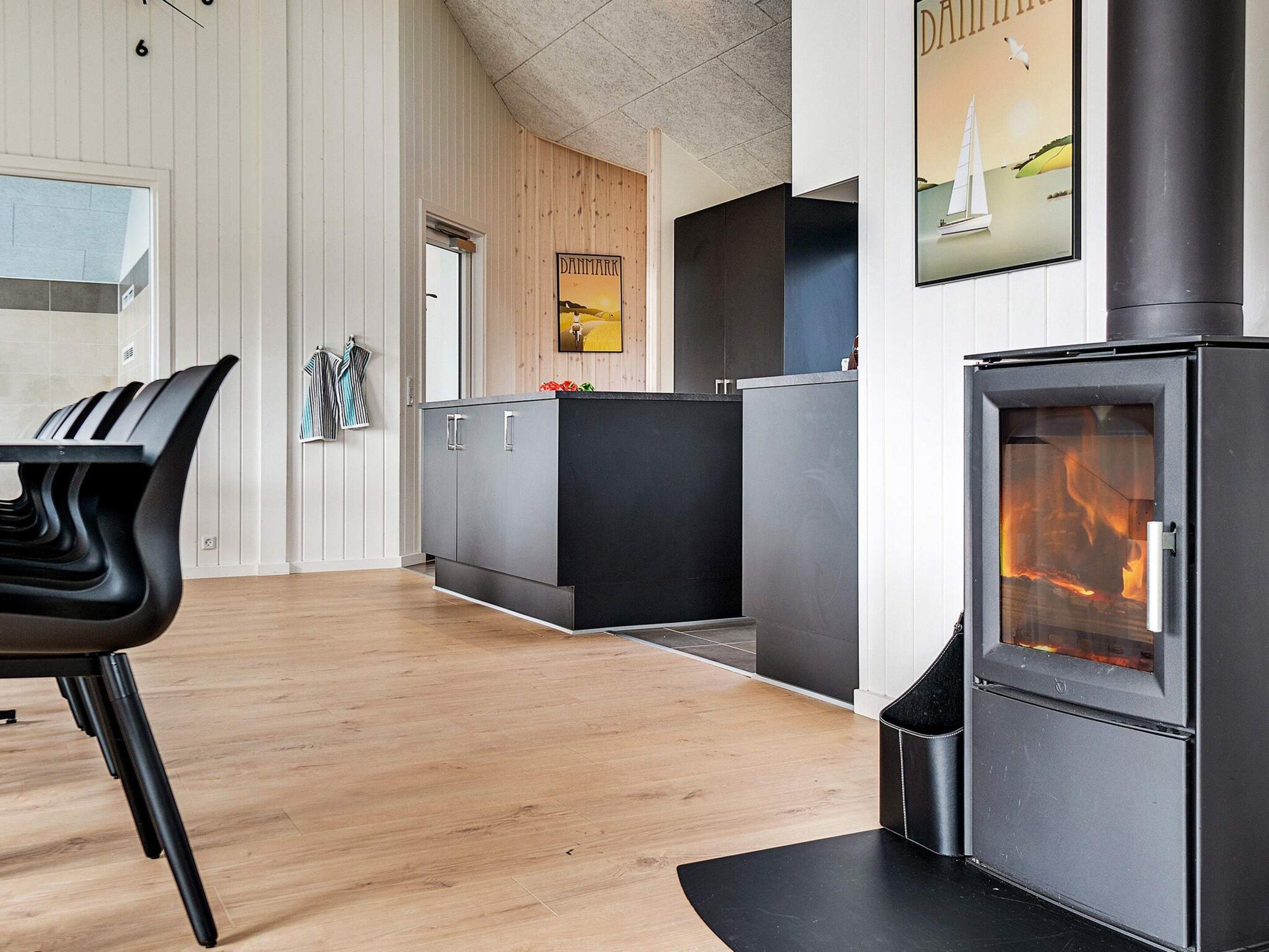 Eine moderne Küche mit Kaminofen, einem Essbereich mit schwarzem Stuhl und einer Holzwand mit einem gerahmten Bild.