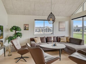 A modern living room with a sectional sofa, a round coffee table, and a hanging light fixture. - 5 Star Holiday Home in Norre Nebel (Norre Nebel)