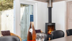 Uma área de estar externa acolhedora, com mesa, cadeiras e uma garrafa de vinho. Uma lareira a lenha é visível ao fundo, transmitindo aconchego.
