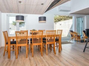 A dining area with a wooden table and chairs, pendant lights, and a view of the outdoors.