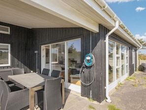 A modern outdoor dining area with a table and chairs, a covered patio, and a charging station.