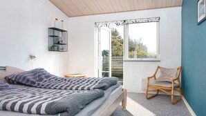 Quarto com cama, cadeira, janela e prateleira na parede.