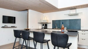 Cozinha moderna com área de bar, teto de madeira e armários brancos.