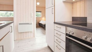 A modern kitchen with white cabinetry, a black countertop, and a built-in oven. There is a window providing natural light and a view of the outdoors. - Holiday Home in Großenbrode (Grossenbrode)