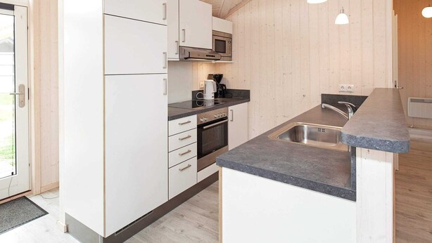 A modern kitchen with white cabinets, a built-in oven, a microwave, and a sink. - Holiday Home in Großenbrode (Grossenbrode)