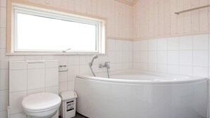 A bathroom with a white bathtub, a toilet, and a window above the sink. - Holiday Home in Großenbrode (Grossenbrode)