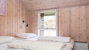A bedroom with wooden walls, a bed with white bedding, a window with a view of trees, and a wall-mounted lamp.