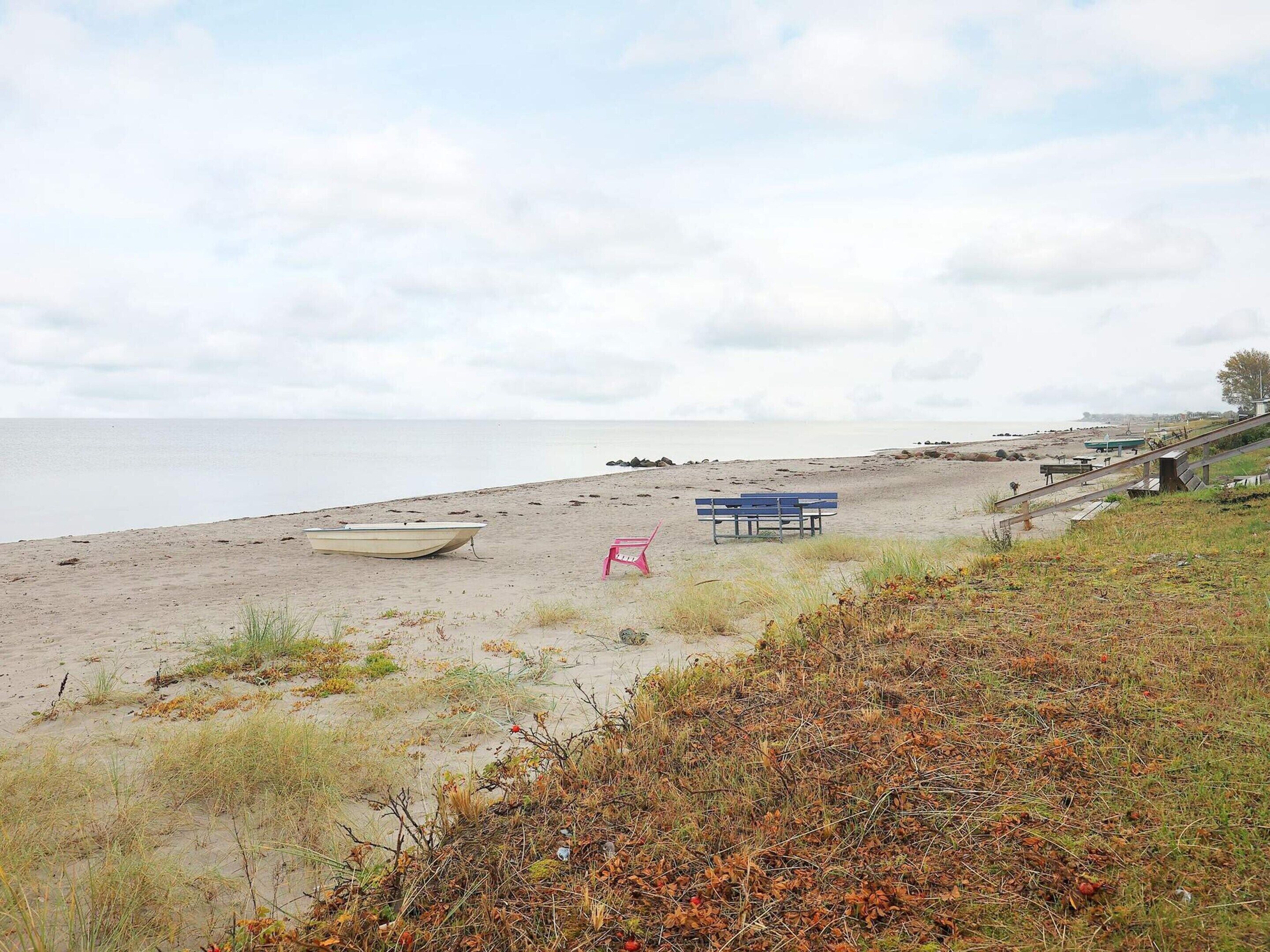 A beach with a boat, a pink chair, and a blue bench.