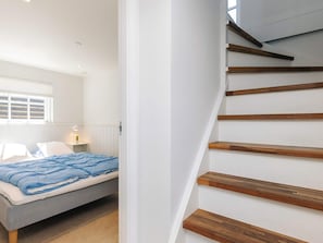 A bedroom with a bed, a nightstand, a window, and a staircase with wooden steps. - 5 Star Holiday Home in Otterup (Otterup)
