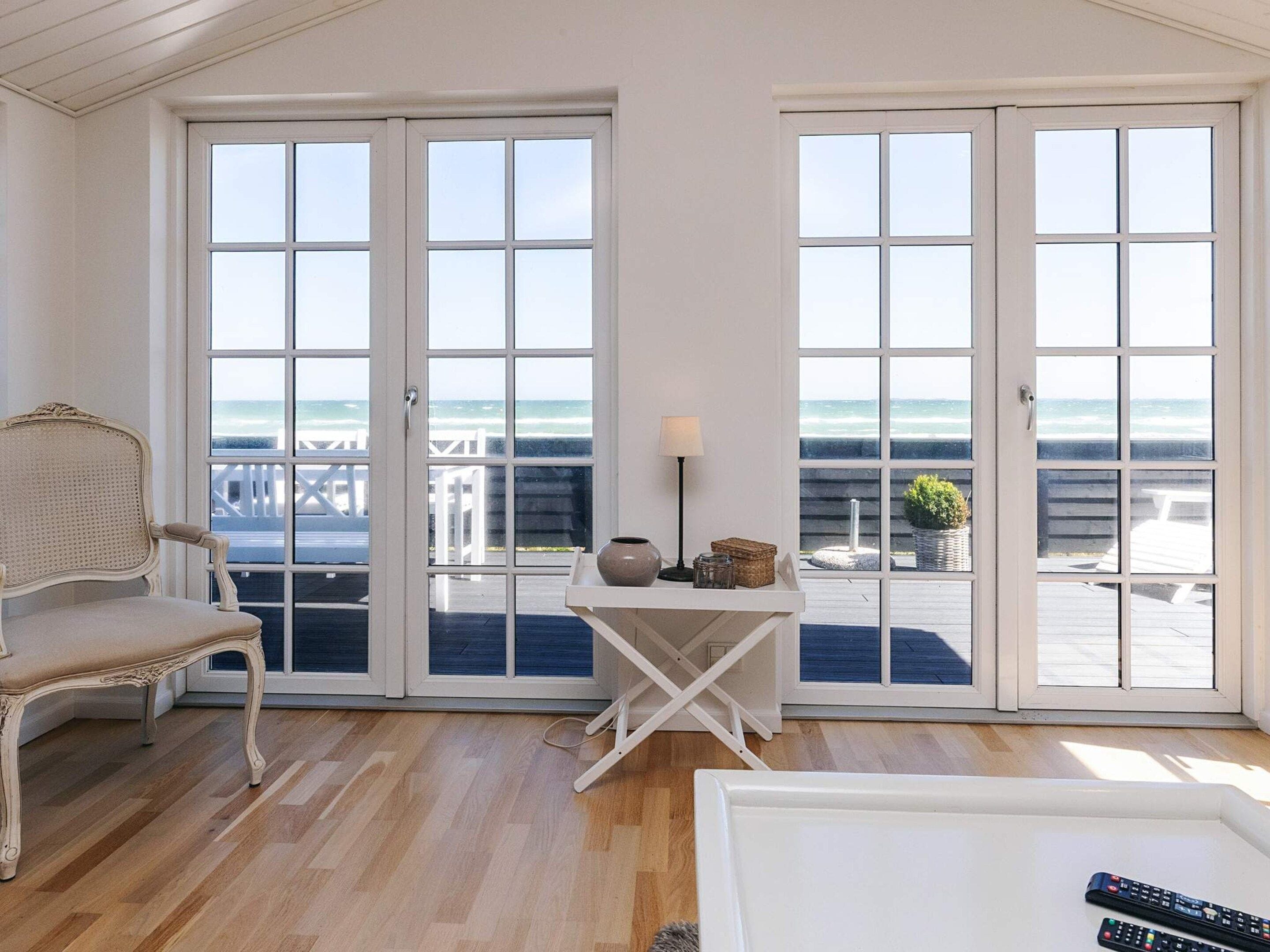 A room with a view of the ocean, featuring a chaise lounge, a small table with a lamp, and a white armchair.