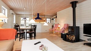 A cozy living room with a fireplace, wooden ceiling, and a dining area with chairs and a table. - 4 Star Holiday Home in Idestrup (Idestrup)