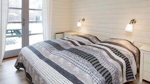 A bedroom with a wooden ceiling, a large bed with patterned bedding, two bedside lamps, and a sliding glass door leading to an outdoor area. - 4 Star Holiday Home in Idestrup (Idestrup)