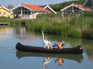 A canoe on calm water with a person and a child, surrounded by houses with red roofs.