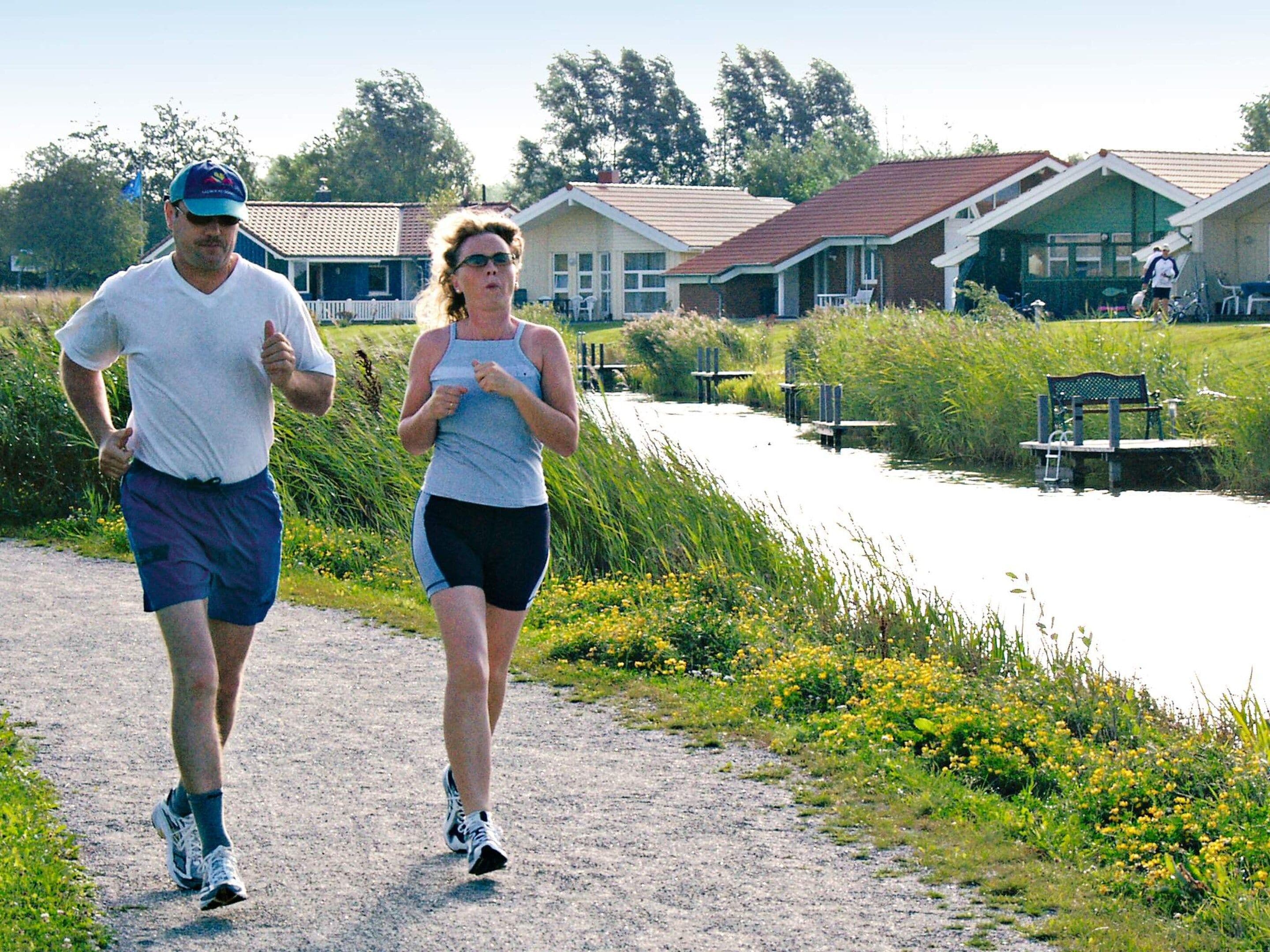 Two people jogging on a gravel path with houses and greenery in the background.