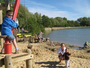 A sandy beach area with wooden play structures and a calm body of water in the background.