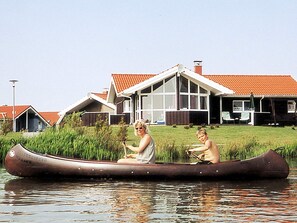 Ein Haus mit rotem Dach und einem großen Fenster, ein Kanu auf dem Wasser und eine Person darin.