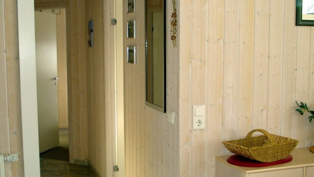 A hallway with wooden walls, a basket on a red base, and a door at the end. - Holiday Home in Otterndorf (Otterndorf)