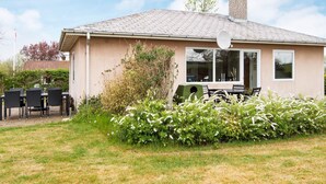 Et etagers hus med tegltag, parabolantenne og en lille have med hvide blomster.