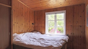 A wooden-paneled room with a bed, a window with a view of greenery, and a door. - 6 Person Holiday Home in Gilleleje (Gilleleje)