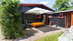 A log cabin with a patio area featuring a table and chairs, a covered seating area, and a small garden. - 6 Person Holiday Home in Gilleleje (Gilleleje)
