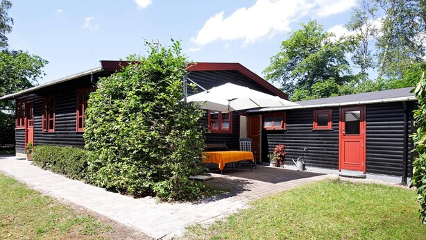 A log cabin with a red door and windows, a covered patio area, and a small garden. - 6 Person Holiday Home in Gilleleje (Gilleleje)
