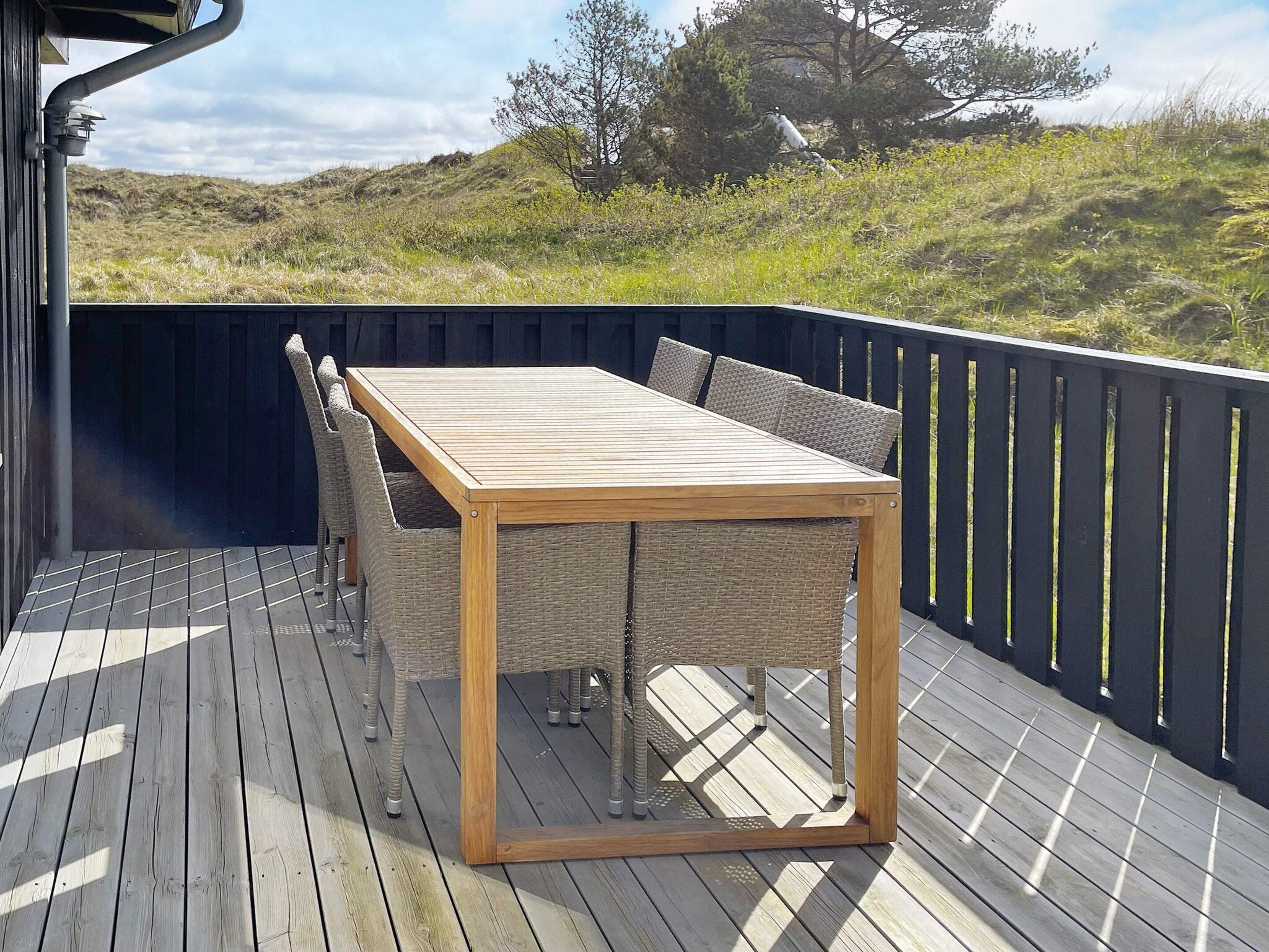 A deck with a wooden table and wicker chairs, overlooking a grassy landscape.