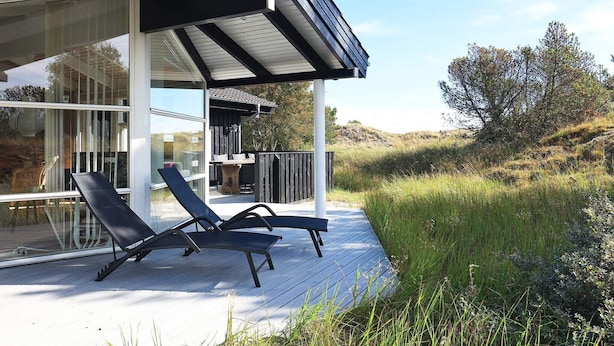A modern outdoor deck with two lounge chairs, a wooden table, and a pergola structure. - 4 Star Holiday Home in Albaek (Aalbaek)