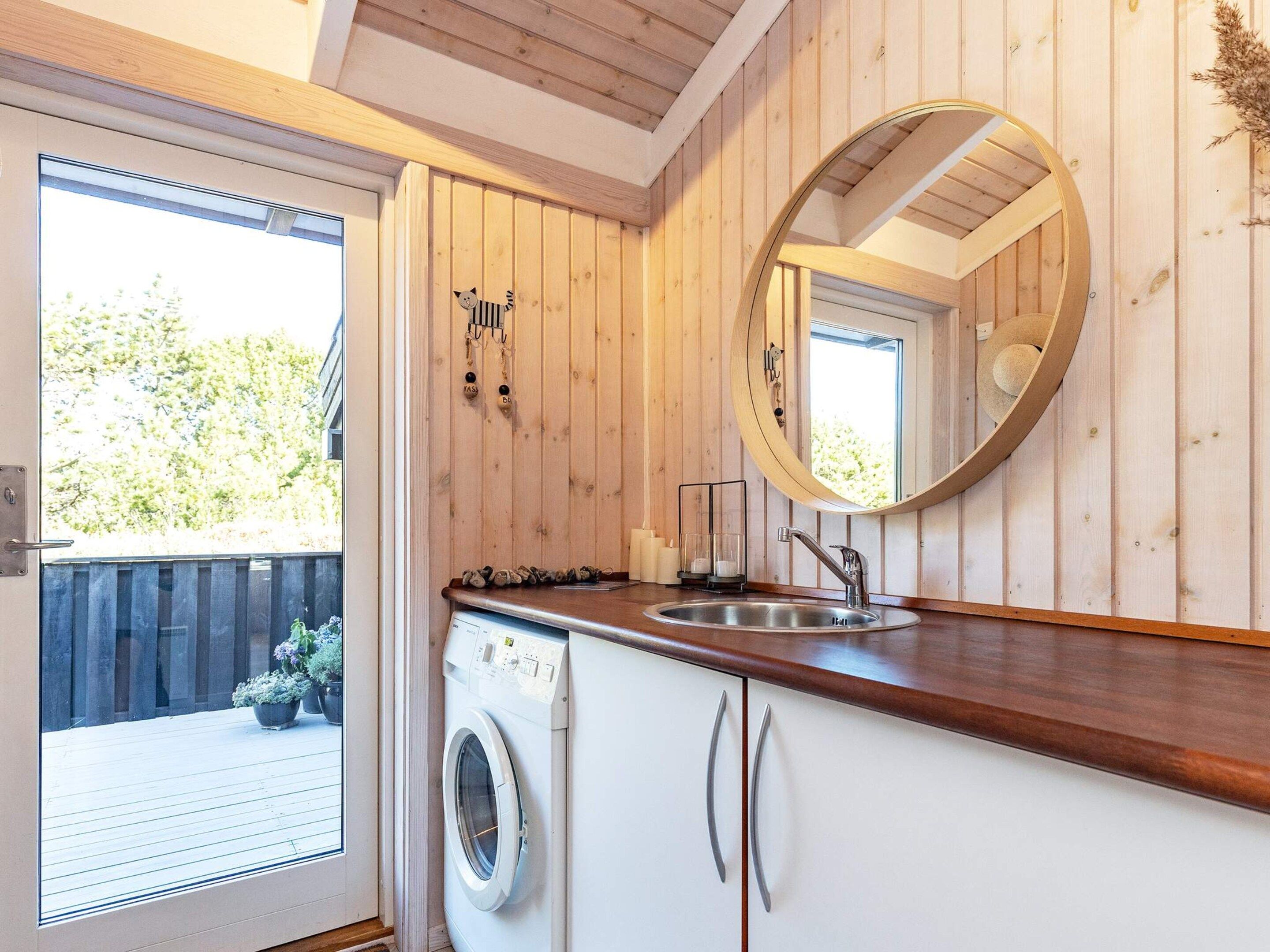 A compact kitchen with a built-in washing machine, a sink, and a large mirror.