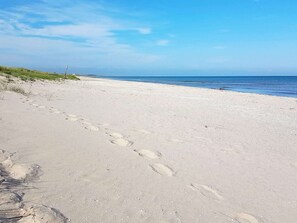 A sandy beach with footprints leading to the water, a clear sky, and a distant horizon.