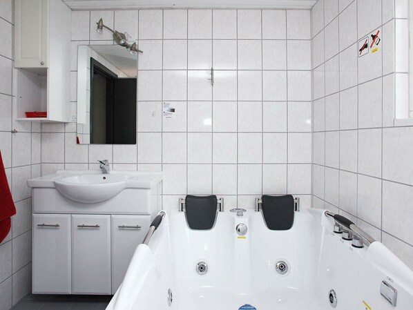 Une salle de bain moderne avec des carreaux blancs, un lavabo blanc, un miroir et une baignoire.