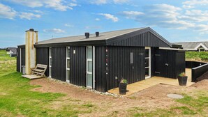 A modern black building with a sloped roof, a chimney, and a wooden deck. - 6 Person Holiday Home in Lokken-by Traum (Lokken)