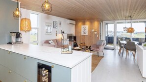 A modern kitchen with a central island, a dining area with a round table, and a cozy seating area with a fireplace. - 6 Person Holiday Home in Lokken-by Traum (Lokken)