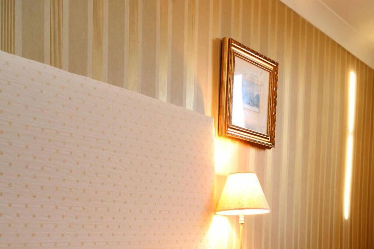 A hotel room with a bed, striped wallpaper, a framed picture on the wall, and a lamp.