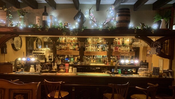 A bar area with wooden chairs, a counter with various bottles and glasses, and decorative lights. - The Horseshoe Inn (Peebles)