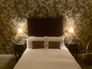 Habitación de hotel con una cama grande, dos lámparas de noche y un papel tapiz estampado.