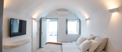 A modern bedroom with a bed, a TV mounted on the wall, and a window providing natural light.