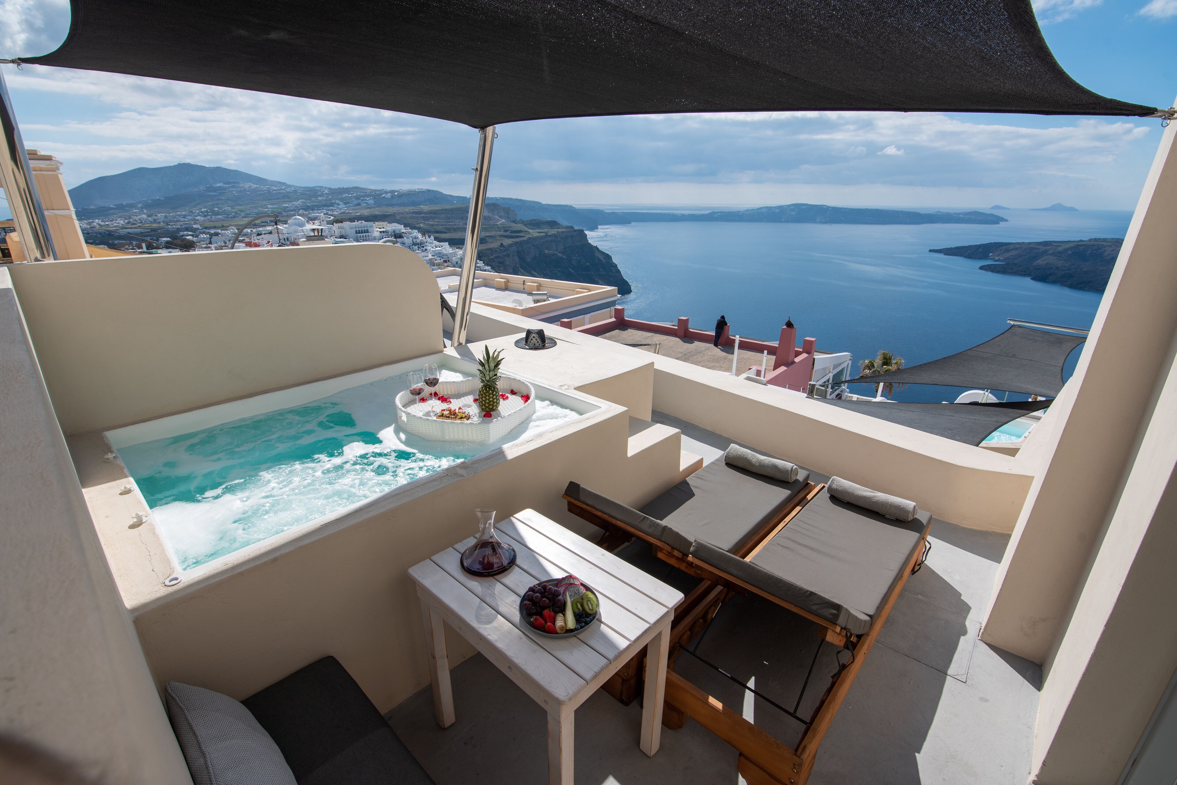 A balcony with a pool, a table with fruit, and a view of the sea and mountains.