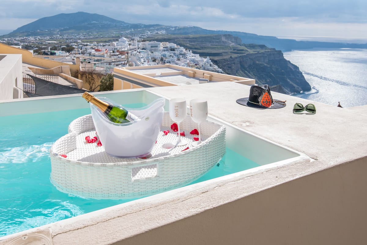 A rooftop pool with a champagne bottle, white furniture, and a view of the coastline.