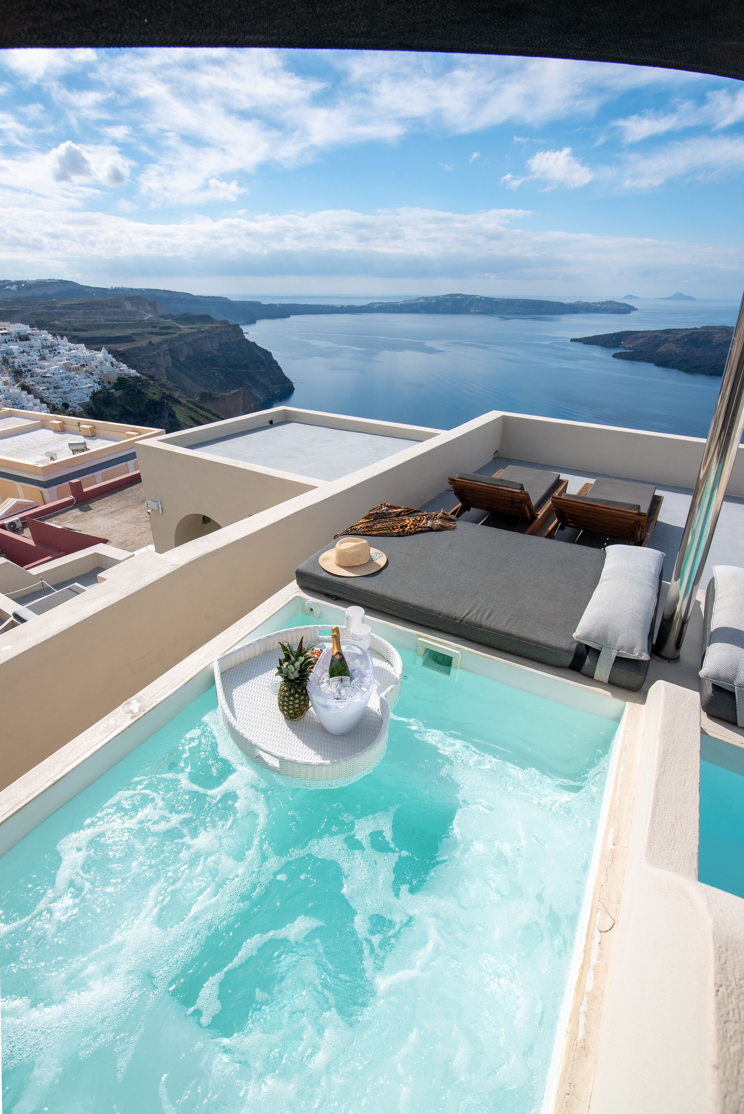 A rooftop infinity pool with a view of the sea, lounge chairs, and a bottle of champagne.