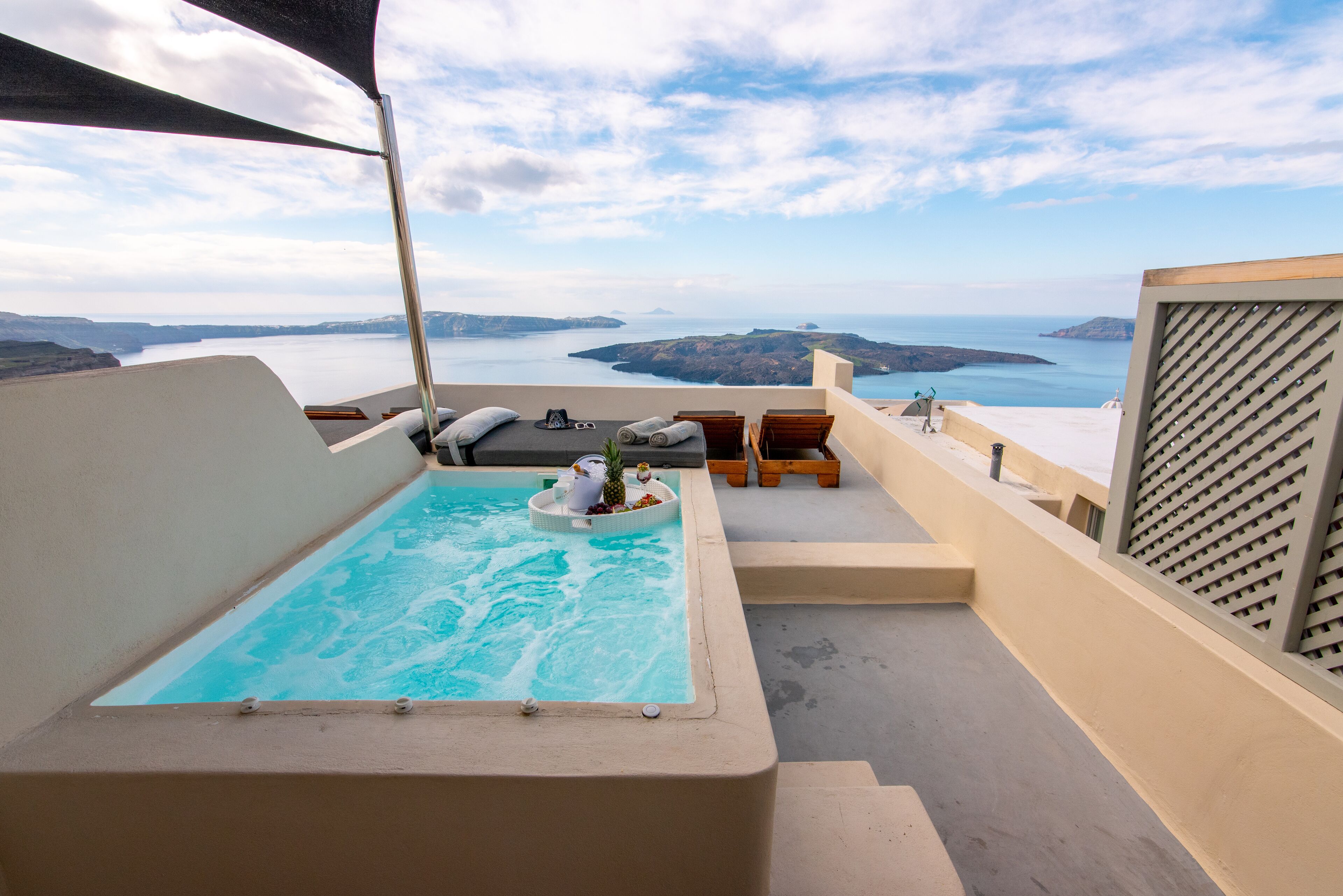 Une piscine sur le toit offrant une vue sur la mer et les îles, entourée de chaises longues et d’une petite table avec des boissons.