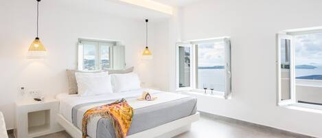 A modern bedroom with a large bed, bedside tables, and a view of the sea.