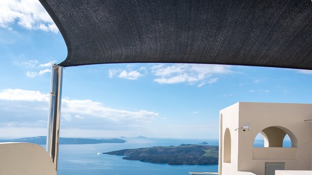A hot tub with a pineapple and rose petals, overlooking a scenic view of the sea and a white building with arches. - Caldera Cliff Illusion (Santorini)