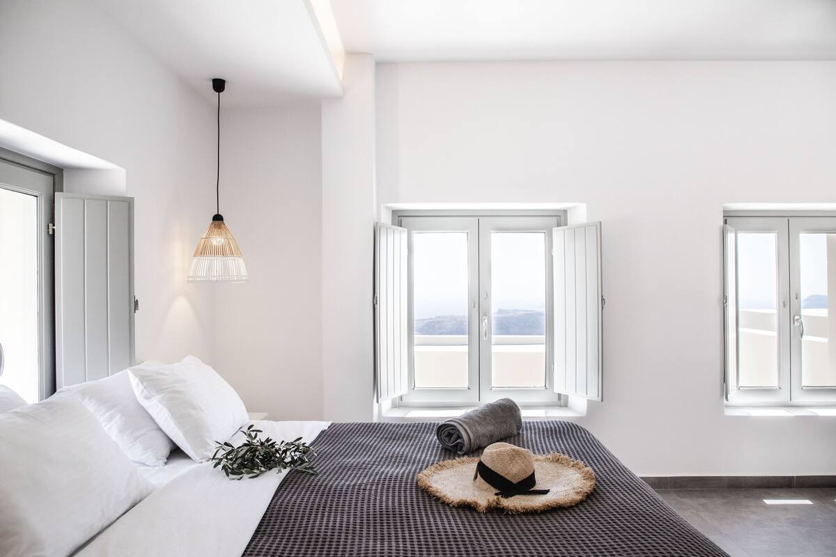 A modern bedroom with a bed, a hanging light fixture, and two windows with a view.