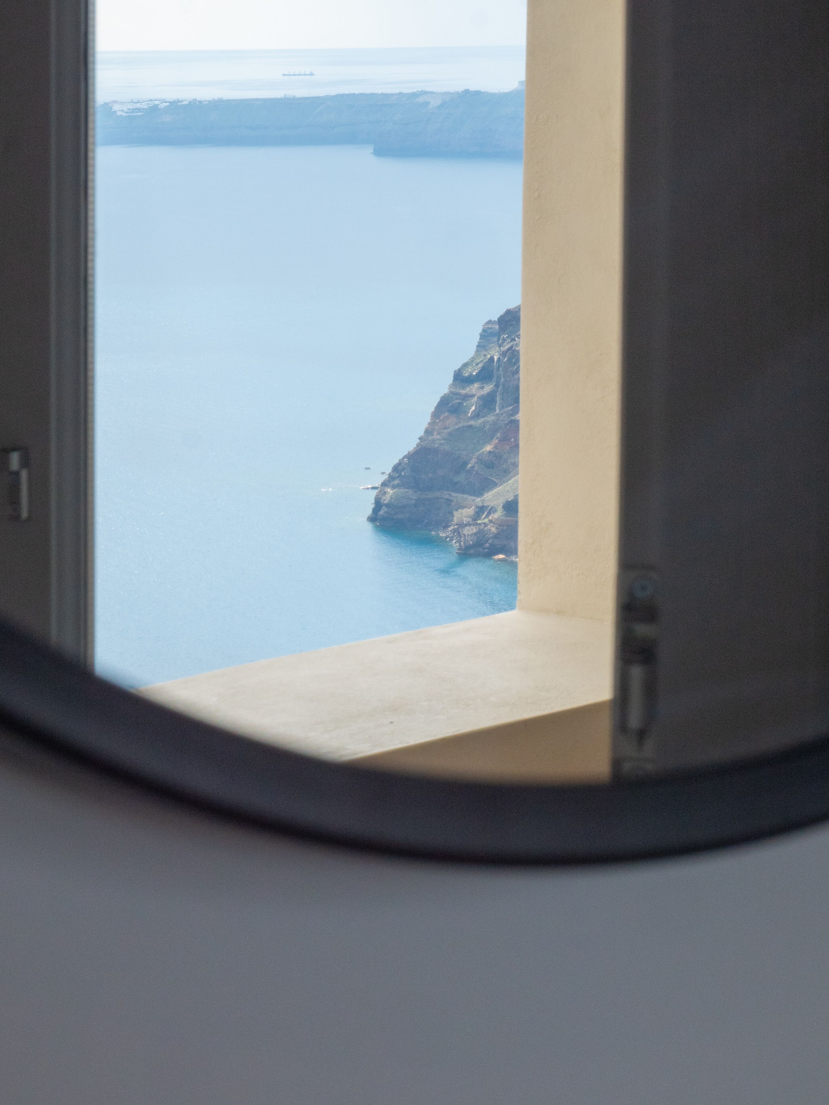 Blick durch ein Fenster auf eine Küstenlandschaft mit einer Klippe und ruhiger See.
