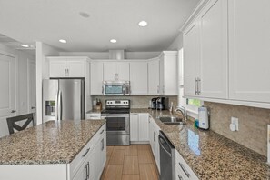 Una cocina moderna con armarios blancos, electrodomésticos de acero inoxidable, encimeras de granito y horno empotrado.