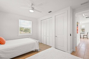 Un dormitorio con cama, ventana con persianas, armario y puerta que da a otra habitación.