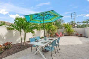 Une terrasse extérieure avec une table et des chaises, un parasol à rayures et des palmiers.