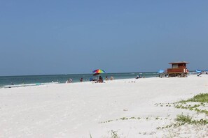 Une plage avec un poste de surveillance pour les sauveteurs, des parasols et des gens.